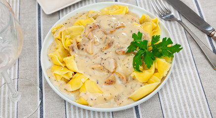 Portion of fresh ravioli is served on plate, drizzled with mushroom sauce. Traditional Italian dough dish with variety of fillings, pour sour cream and mushroom gravy, leaf of parsley