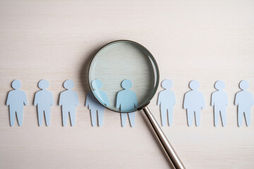 Paper people figures in row. Magnifying glass focuses on one figure. Job search concept. Hiring process. Finding best candidate. Recruitment. Headhunting. Human resources. Candidate selection.