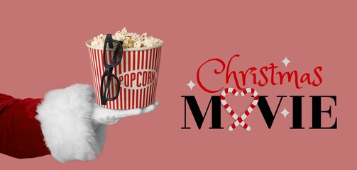 Santa's hand with bucket of popcorn and 3D glasses on pink background. Christmas movie concept