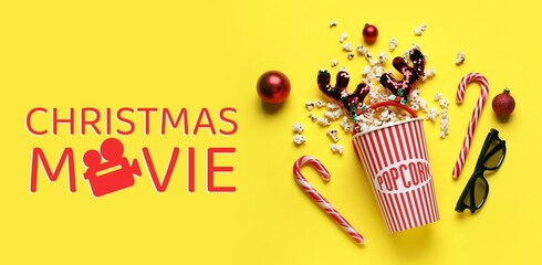 Bucket of popcorn, 3D glasses and decorations on yellow background. Christmas movie concept