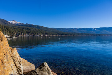 a gorgeous winter landscape at Lake Tahoe with blue lake water, lush green trees and plants and snow capped mountains at sunrise in Crystal Bay Nevada USA
