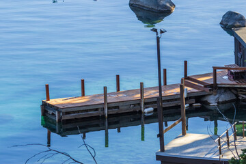 a brown wooden boat dock over the rippling water of Lake Tahoe at Crystal Bay with trees and rocks...