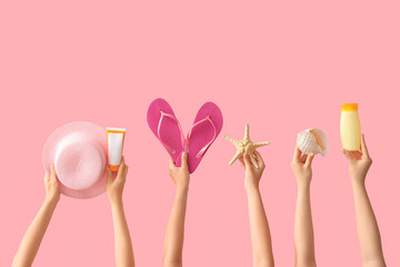 Female hands with beach accessories and flip-flops on pink background