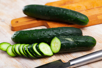 Whole and sliced fresh cucumbers on wooden table. Healthy vegetarian ingredient