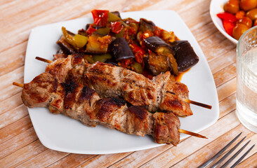 Spicy grilled pork meat skewers served with eggplant and tomato saute
