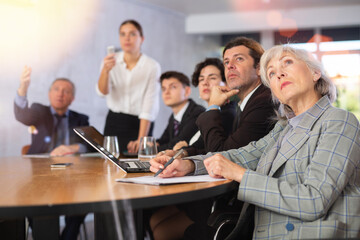 Focused mature female entrepreneur attending training in office watching attentively presentation of business coach..