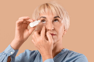 Mature woman using eye drops on beige background