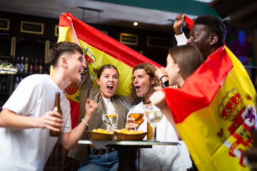 Group of Spain football team fans spending time in bar, drinking bear and having fun. People with state flag in pub.