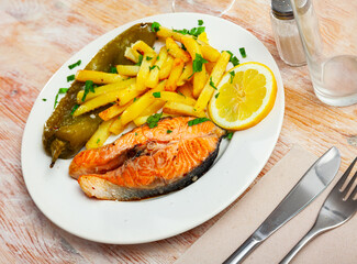 Fresh salmon steak with roasted green pepper and fried potato served on table with serving pieces.