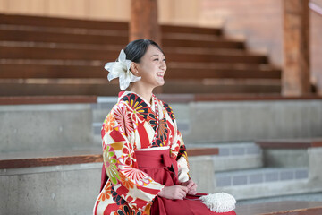 Japanese woman in her 20s wearing red hakama, staple for Japanese university graduates, sits in...