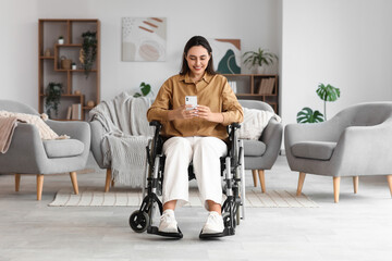 Young woman in wheelchair using mobile phone at home