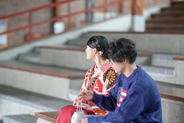 A Japanese woman in her 20s wearing a red hakama, a staple for Japanese university graduates, and a teenage man wearing casual clothes are sitting in a room.
