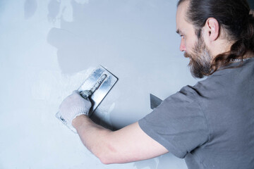 A person smoothly spreads microcement on a wall using a trowel in a workshop setting.