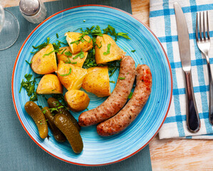 Appetizing fried frankfurters with vegetable garnish of boiled potatoes in their skins, pickles and fresh greens