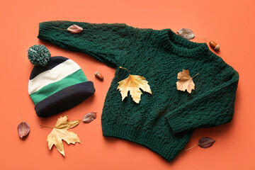 Composition with warm children's sweater, hat, acorns and fallen leaves on color background
