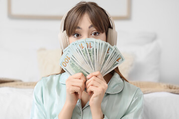 Young woman with headphones and dollar banknotes in bedroom, closeup