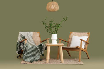 Table with bamboo stems in vase, armchairs and lamp on green background