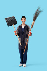 Male scavenger with snow shovel and broom on blue background
