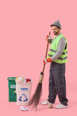 Male scavenger with broom and trash bins on pink background
