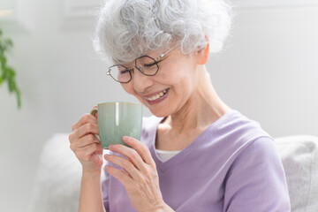 ソファーでコーヒーを飲みながらくつろぐシニア女性