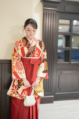 Fototapeta premium A Japanese woman in her 20s stands in front of an interior door wearing a red kimono (hakama), a staple of Japanese university graduates.