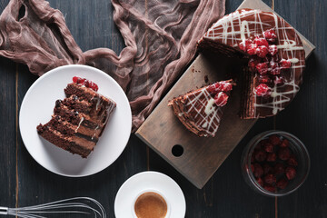 A slice of cake with chocolate and cherry on a plate. Cup of espresso and cake on a wooden board. Top view.