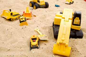 yellow toy excavators and trucks on sand in a childrens sandbox