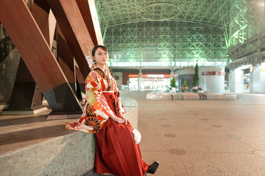A Japanese woman in her 20s sits at an illuminated train station in Kanazawa, Ishikawa Prefecture, wearing a red kimono (hakama), a staple for Japanese university graduates.