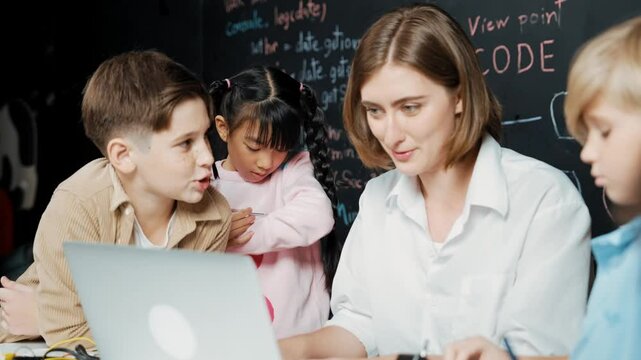 Caucasian teacher using laptop and explain about engineering system while diverse student holding electronic equipment in front of blackboard with prompt or code written in STEM class. Erudition.