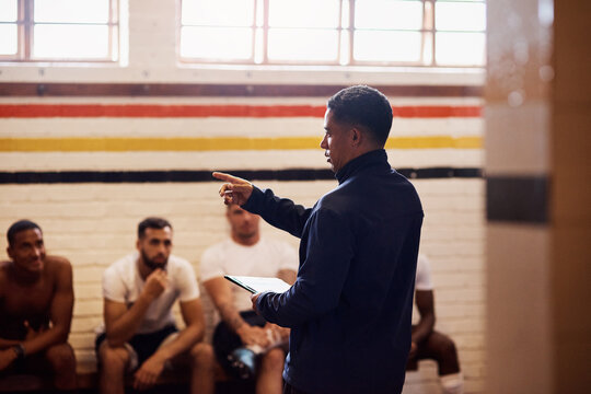 Men, coach and discussion with sports team in locker room for game plan, formation or meeting. Male people, trainer and brainstorming strategy with group for pitch, presentation or half time break