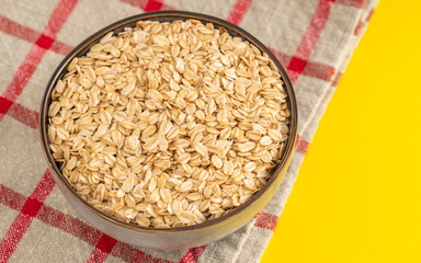 Rustic bowl filled with rolled oats on a checkered cloth with a yellow background. Ideal for breakfast and healthy eating themes.