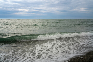 An incoming wave on the Black Sea and a pebble beach on the Sochi coast on a summer day with clouds, Sochi, Krasnodar Territory, Russia