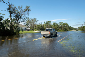 Hurricane flooded street with moving cars in surrounded with water Florida residential area. Consequences of natural disaster