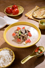Soto Betawi is a creamy, coconut milk-based soup from Jakarta Indonesia, featuring beef or offal, potatoes, and spices, served with rice, lime, and sambal - selective focus