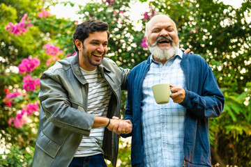 Indian Asian Old aged father and young adult son walking in a home garden with coffee