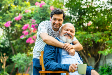 Indian Asian Elderly father, young son embracing with joy in the home garden, showcasing loving bond