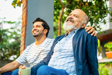 Indian Asian Elderly father and adult son enjoying a cheerful conversation on the porch, bonding