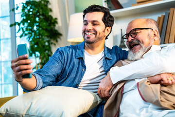 Indian Asian Senior father, young son sharing smiles while speaking on a video call in a modern home