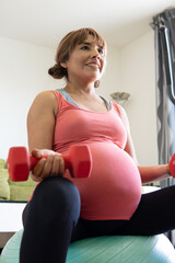 close-up pregnant woman about to give birth performing prenatal exercises with dumbbells sitting on a yoga ball. Ready to give birth. Concept: pregnancy, maternity, fertility, prenatal exercises.