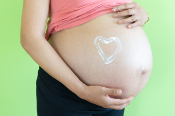 belly young pregnant woman unrecognizable applying moisturizing cream of stretch marks on the belly, heart-shaped. skin care concept during pregnancy and maternity.