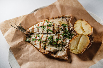 sea bream fish fillet seasoned with sauce, mediterranean herbs, served with baked potatoes on parchment cooking paper and plate