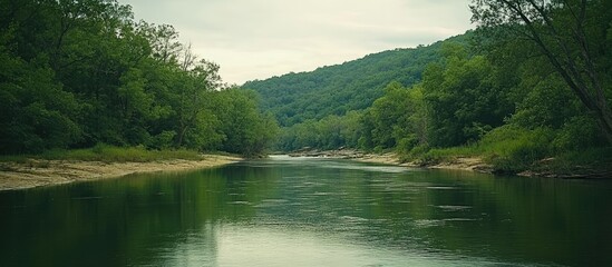 Serene river landscape with lush greenery and foothills under a cloudy sky in a tranquil natural setting.