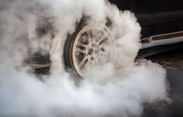 Smoke on wheel of drag race car at start line.