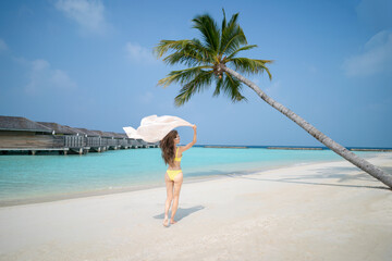 Woman in yellow bikini posing under the coconut trees on tropical beach.