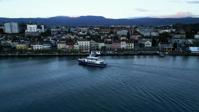 Push in drone shot of boat arriving in Nyon port at sunrise with cityscape in Canton of Vaud Switzerland