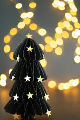 A black paper tree with stars on it is lit up by a light. The tree is surrounded by a blurry background, giving the impression of a dreamy, ethereal atmosphere