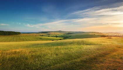Obraz premium Sunset and sunrise over a peaceful countryside field with green grass, distant mountains, and a blue sky filled with clouds