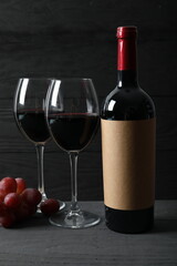 Fototapeta premium Bottle of red wine with grapes, corkscrew and corks on wooden background