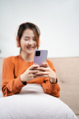 Happy woman, headphones and smartphone in living room on social media app, audiobook or radio podcast on sofa. Young girl, mobile music and listening to audio, streaming and singing in home lounge