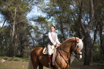 Obraz premium portrait of equestrian woman, young and beautiful, riding and holding the reins of her purebred brown horse with blond mane and tail. The woman is happy. Concept of love for the horse.
